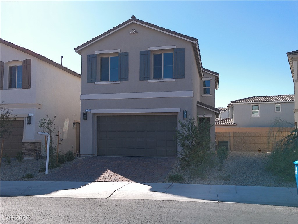 View of front of house featuring a garage, stucco siding, and decorative driveway