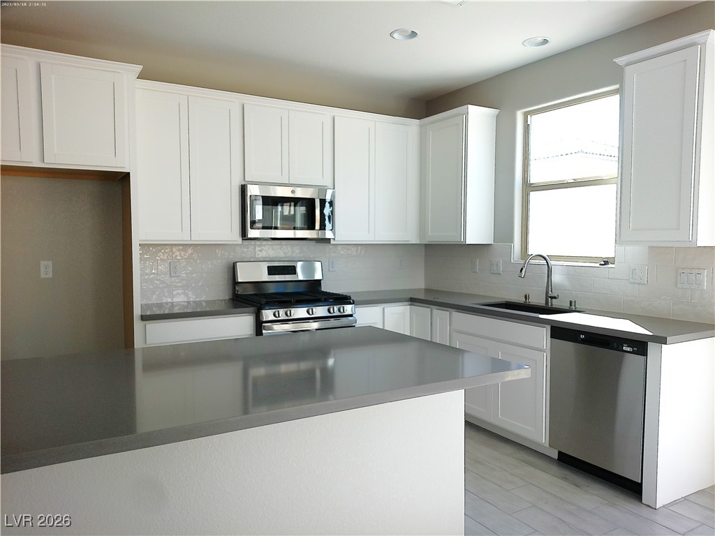 6607 Dove Point Place Las Vegas, NV 89130 - Photo 3 of 14 Kitchen with stainless steel appliances, white cabinetry, tasteful backsplash, and light wood-type flooring