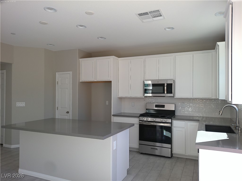 6607 Dove Point Place Las Vegas, NV 89130 - Photo 4 of 14 Kitchen with stainless steel appliances, a kitchen island, white cabinets, backsplash, and recessed lighting