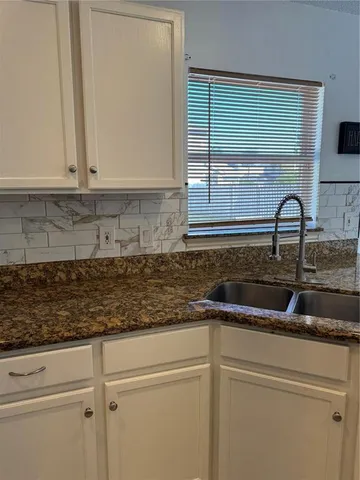 a kitchen with granite countertop a sink and a white cabinets