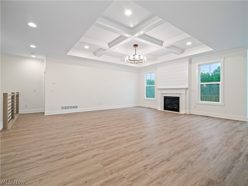 32 Brookside Lane North Ridgeville, OH 44039 - Photo 26 of 50 Unfurnished living room featuring a chandelier, light wood-type flooring, coffered ceiling, a glass covered fireplace, and beamed ceiling