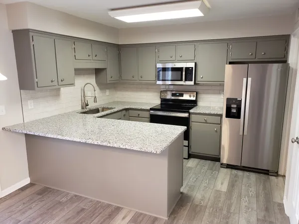 a kitchen with stainless steel appliances granite countertop a refrigerator a sink dishwasher a stove top oven a refrigerator and white cabinets with wooden floor