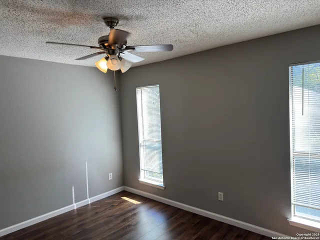 an empty room with wooden floor chandelier fan and windows