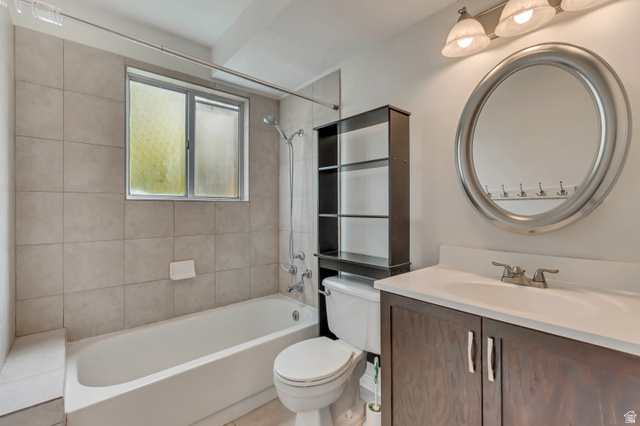 653 South 500 West, Unit 1 Provo, UT 84601 - Photo 14 of 17 Bathroom featuring a single vanity with a wood-finish cabinet and white countertop, an oval mirror, a three-light fixture, a tub/shower combination with light-toned wall tiling, and a window with obscured glass
