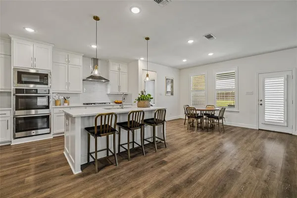 a kitchen with stainless steel appliances a stove a sink a oven a dining table and chairs with wooden floor