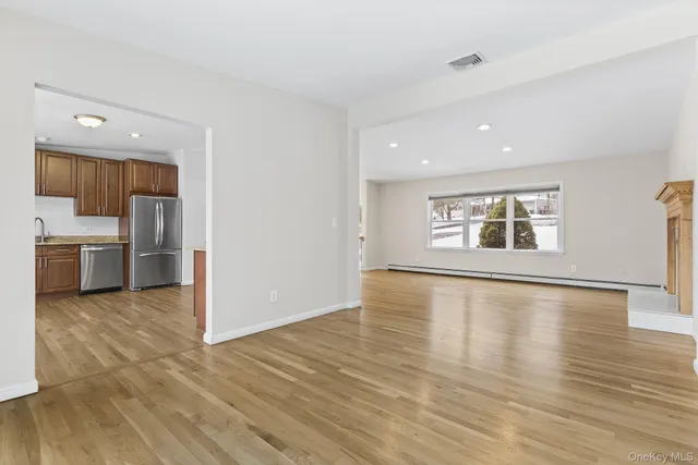 an empty room with wooden floor kitchen view and windows