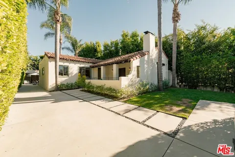 a front view of a house with lots of trees and flowers around