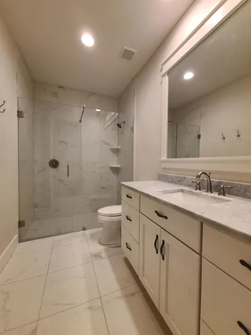 a bathroom with a granite countertop sink a toilet a mirror and shower