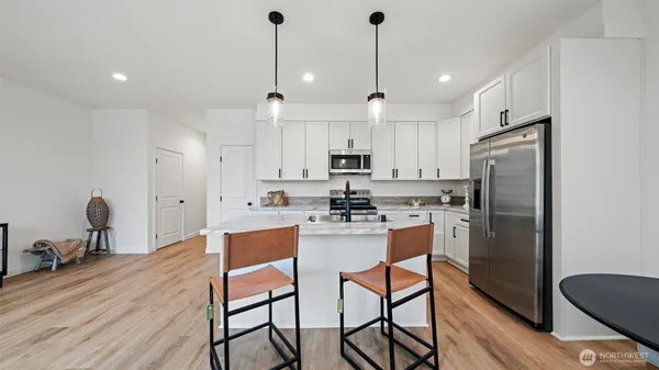 a kitchen with stainless steel appliances kitchen island granite countertop a refrigerator a stove a sink dishwasher with a dining table and chairs with wooden floor