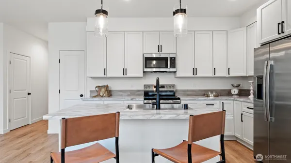 a kitchen with stainless steel appliances granite countertop a stove a sink a microwave a refrigerator and white cabinets