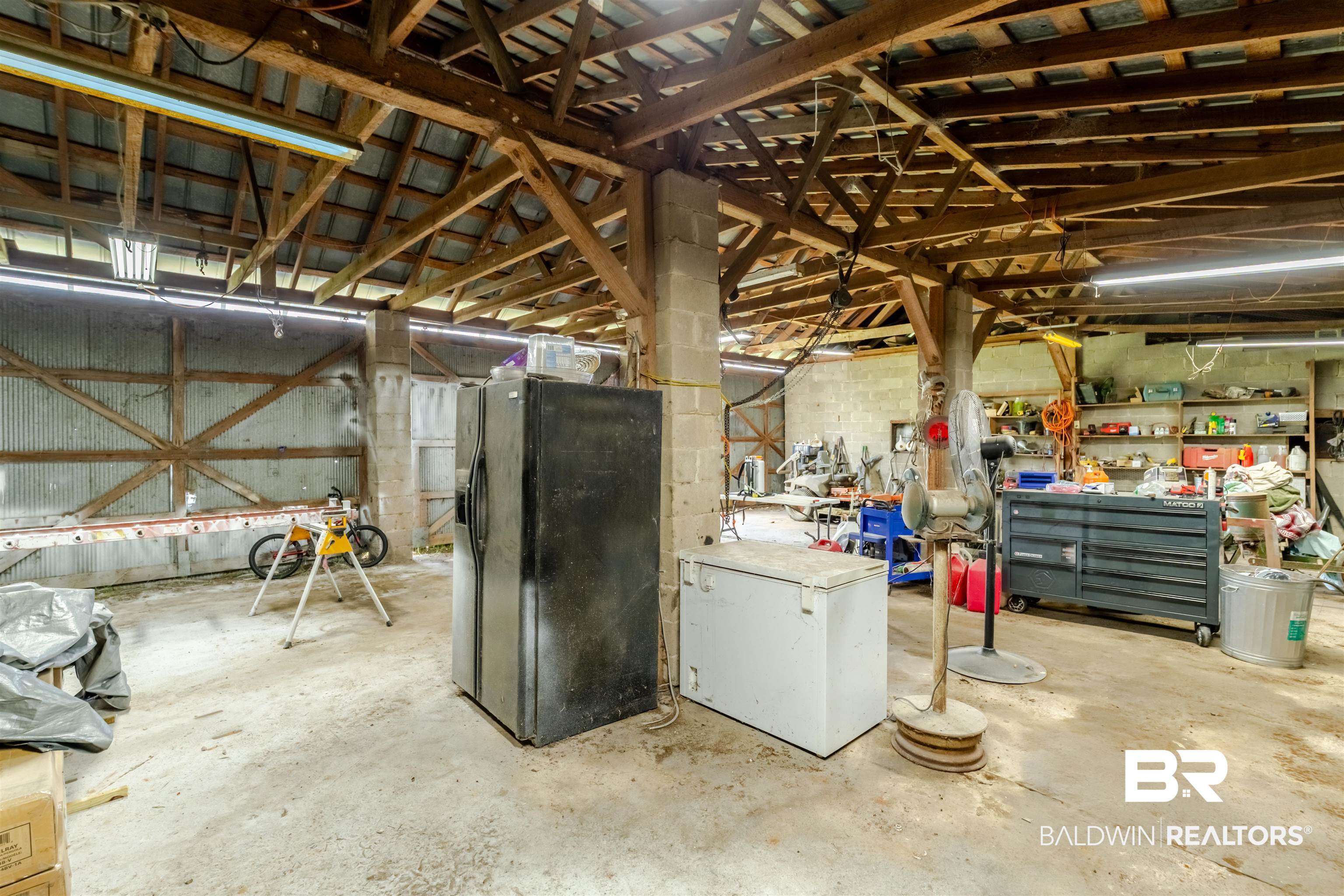 15575 Mikkelsen Road Summerdale, AL 36580 - Photo 45 of 68 Spacious utilitarian interior featuring exposed wood beams, concrete flooring, fluorescent lighting, and corrugated metal wall panels