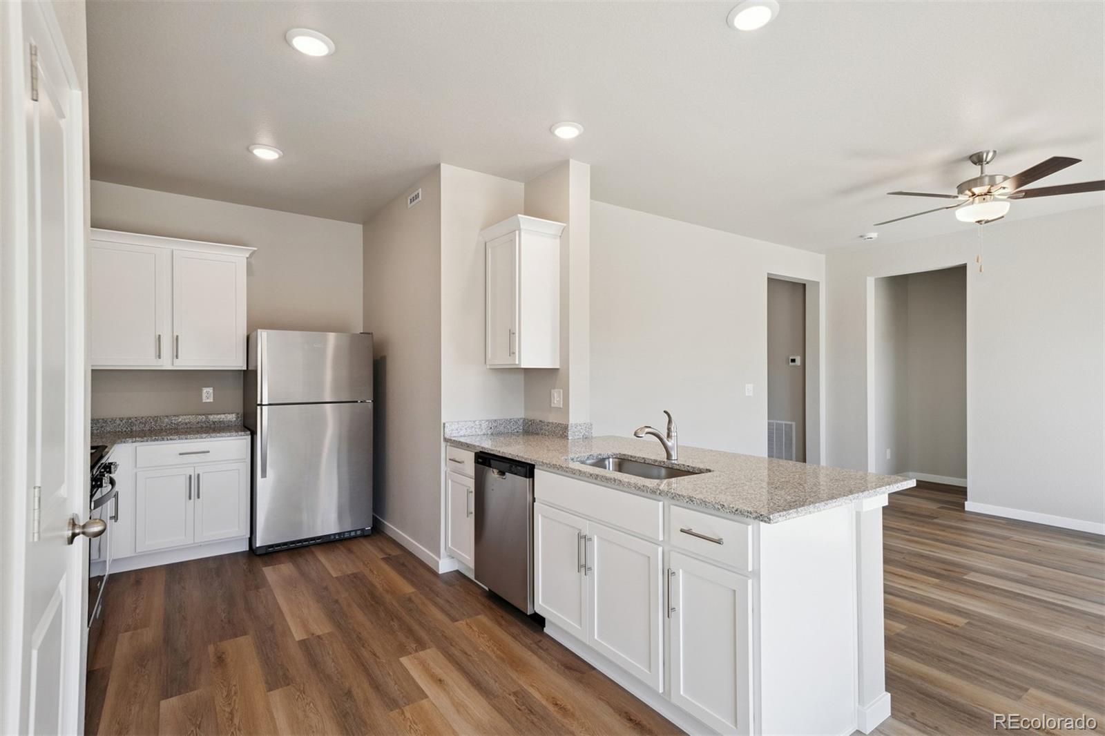 2144 Alyssa Street Fort Lupton, CO 80621 - Photo 3 of 38 a kitchen with a sink a refrigerator a stove and white cabinets with wooden floor