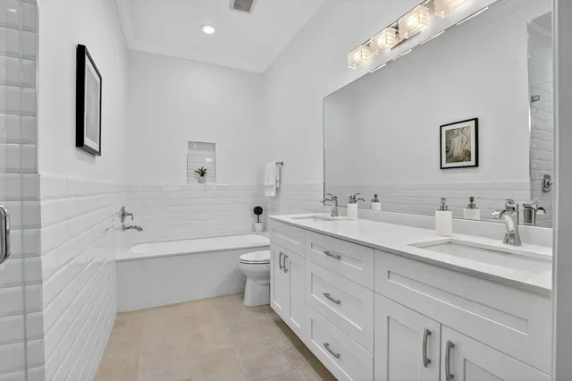 a bathroom with a double vanity sink a toilet a bathtub and shower