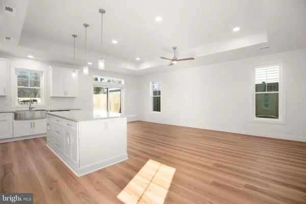 a large kitchen with kitchen island a stove a sink a refrigerator and white cabinets with wooden floor
