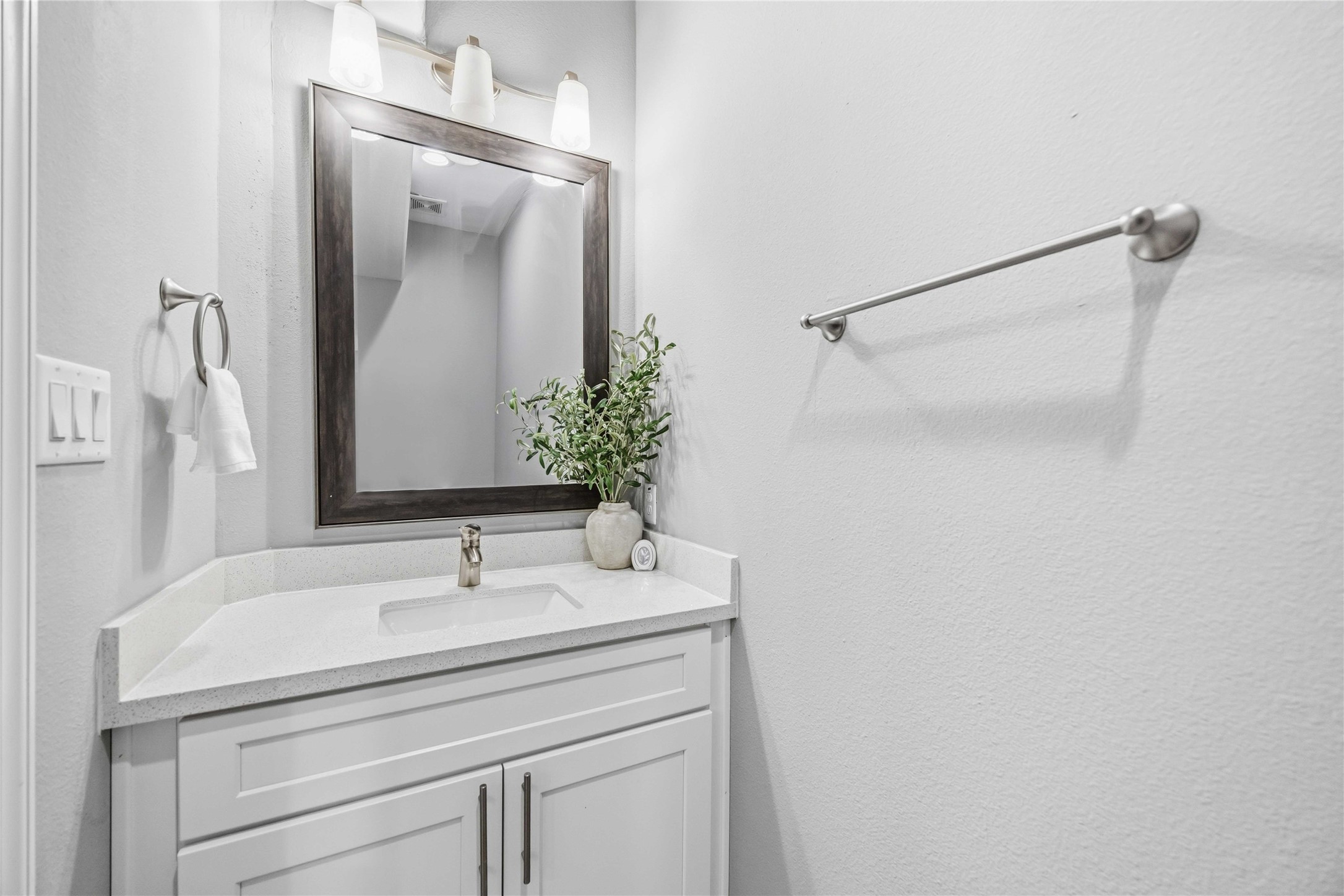 4903 Mallow Street, Unit A Houston, TX 77033 - Photo 4 of 10 Bathroom features a white vanity cabinet and white stone countertop. A large, dark-framed rectangular mirror hangs above the sink, topped by a three-bulb vanity light fixture with frosted white glass shades