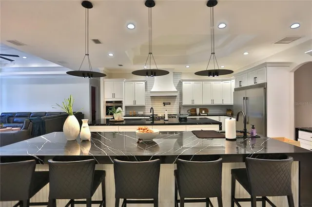 a kitchen with stainless steel appliances granite countertop a sink a stove a refrigerator and chairs