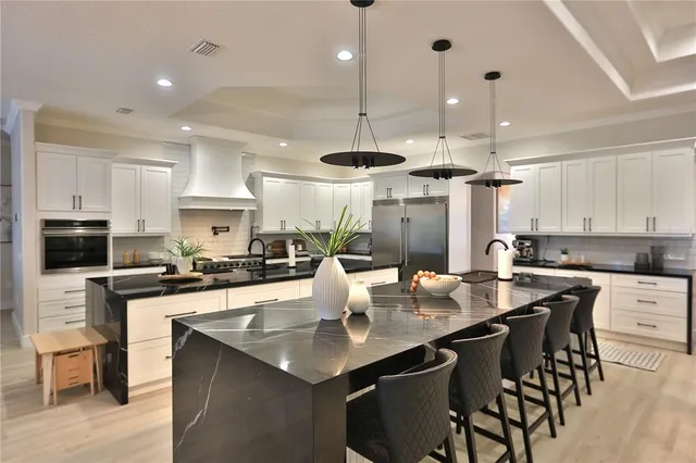 a kitchen with stainless steel appliances granite countertop a sink a stove a kitchen island with chairs and white cabinets
