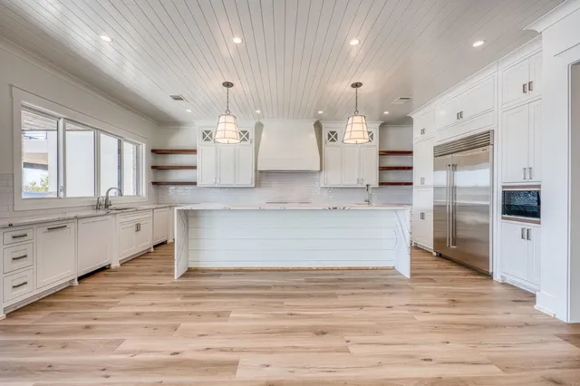 a large white kitchen with kitchen island a refrigerator wooden floor and a counter top