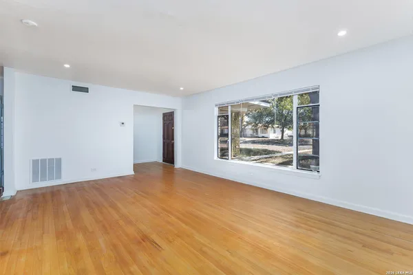 a view of an empty room with wooden floor and a window