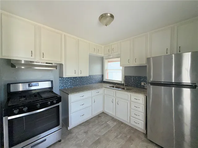 a kitchen with granite countertop a refrigerator stove and white cabinets