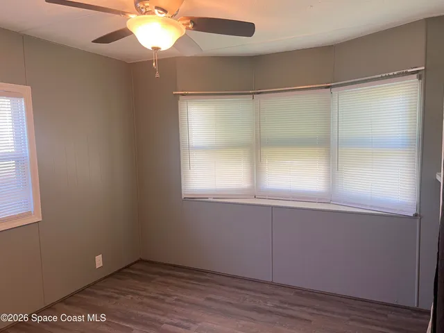 an empty room with wooden floor fan and windows
