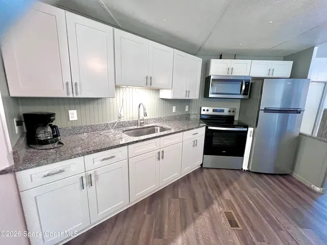 a kitchen with stainless steel appliances granite countertop a refrigerator a sink a stove and white cabinets with wooden floor