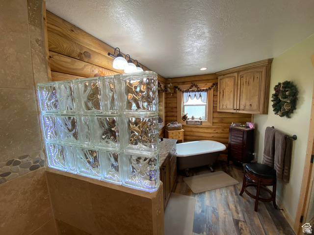 79 Auburn Forest Road Auburn, WY 83111 - Photo 34 of 76 Bathroom featuring rustic walls, a textured ceiling, a freestanding tub, dark wood-type flooring, and vanity