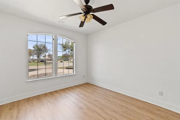 an empty room with wooden floor fan and windows