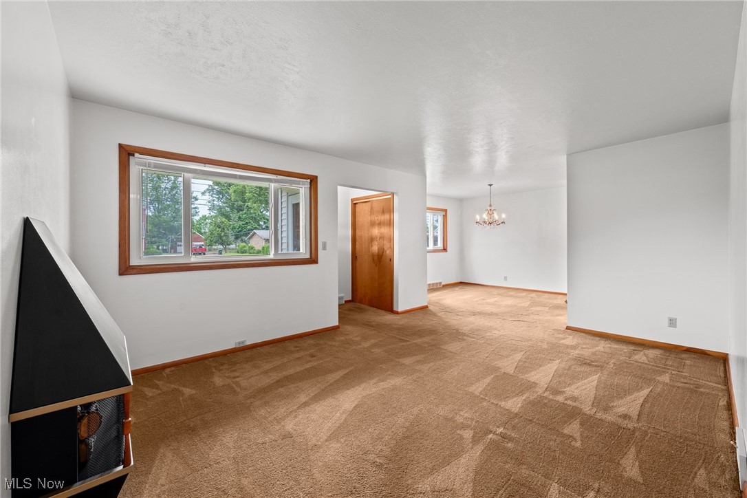 Carpeted empty room featuring a chandelier and baseboards