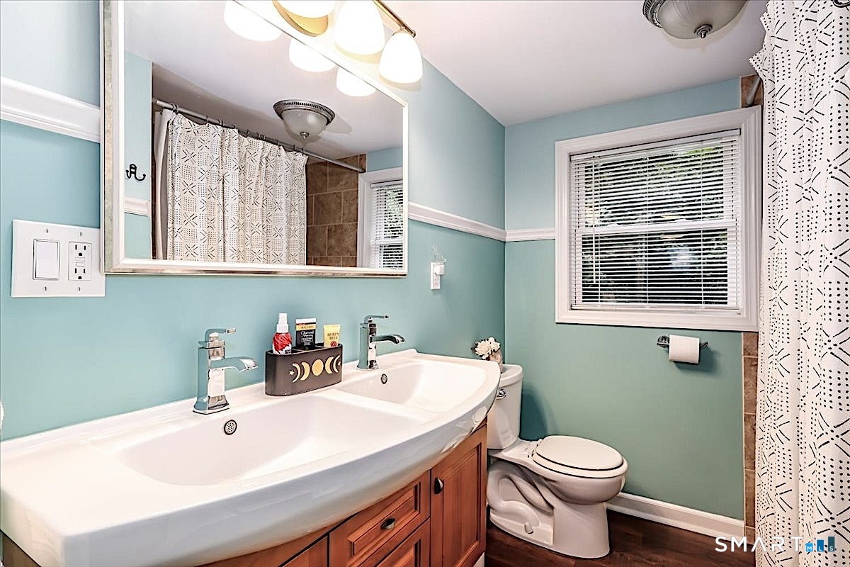313 Torrington Road Litchfield, CT 06759 - Photo 18 of 26 Second Level Bath Featuring a Double-Sink Vanity, Warm Wood Cabinetry, Tiled Shower, and a Window Offering Natural Light and Leafy Views