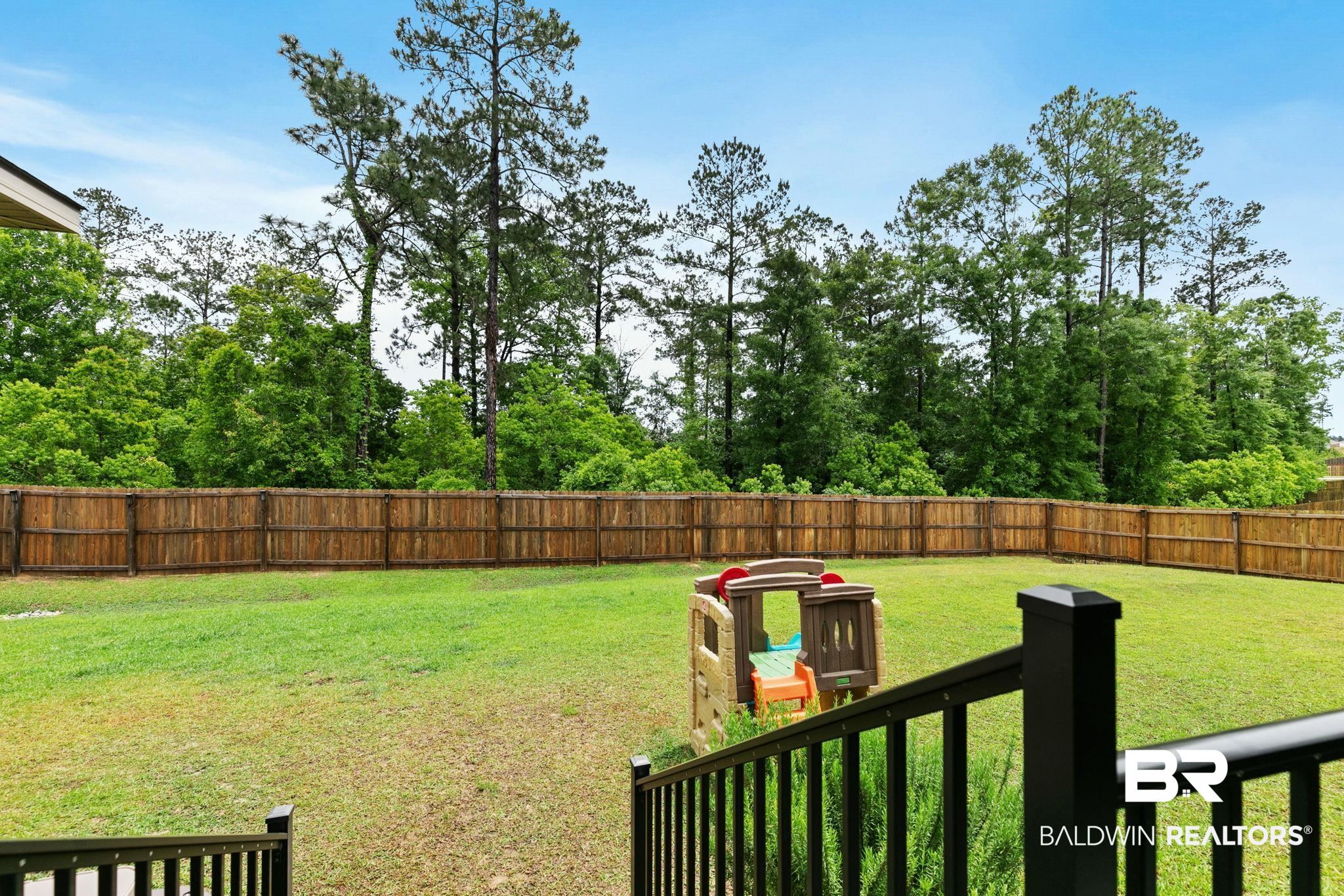 13233 Ibis Boulevard Daphne, AL 36527 - Photo 55 of 100 Expansive green lawn enclosed by a tall wood privacy fence, backed by mature trees