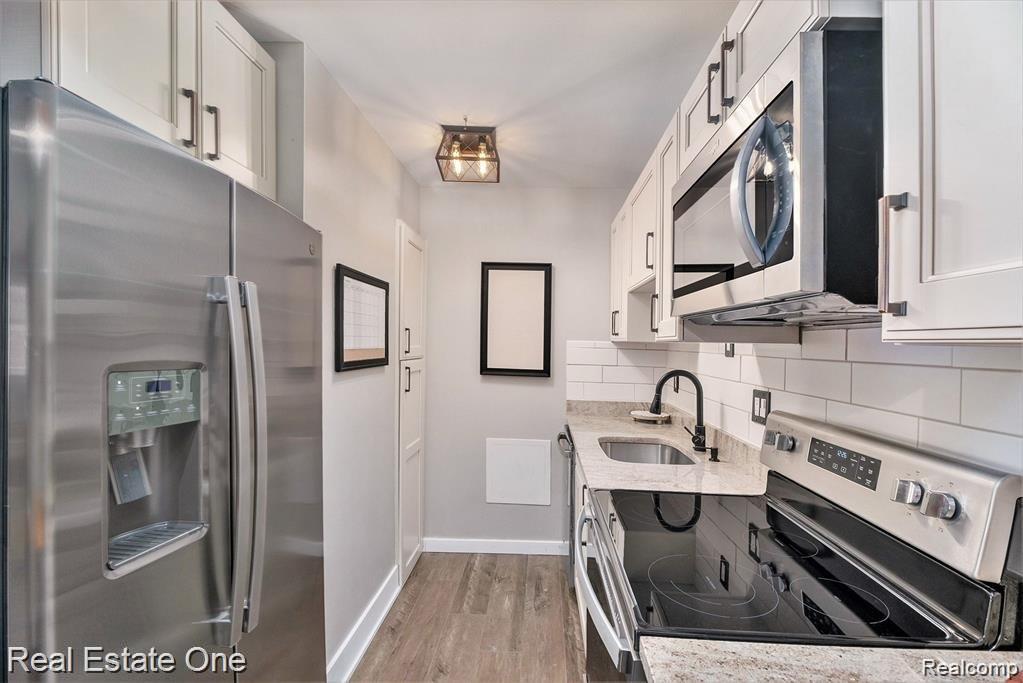 803 Plate Street, Unit 104 Rochester, MI 48307 - Photo 11 of 14 Galley kitchen featuring stainless steel appliances, white shaker cabinetry, granite-style countertops, subway tile backsplash, and wood-finish flooring