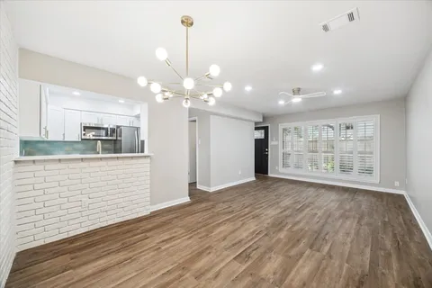 a view of an empty room with wooden floor and kitchen view