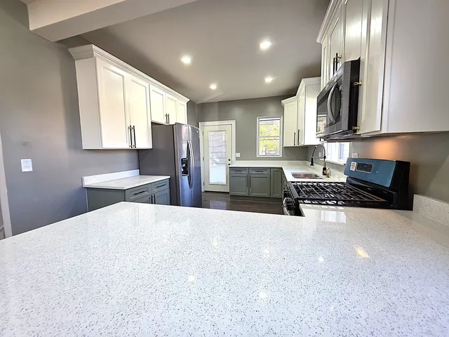 a large kitchen with stainless steel appliances a large counter top a stove a sink a refrigerator and cabinets