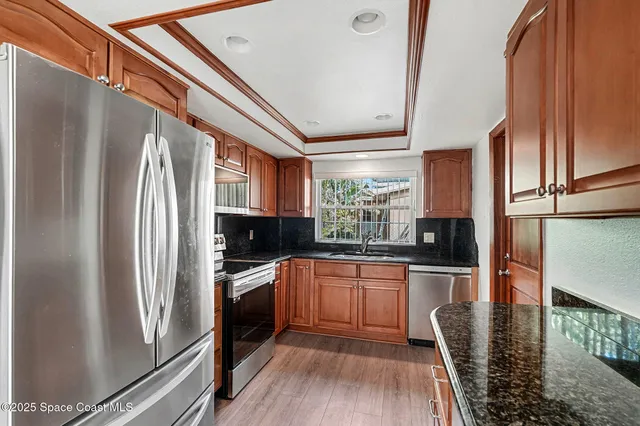 a kitchen with stainless steel appliances granite countertop a refrigerator a stove and a sink with wooden floor