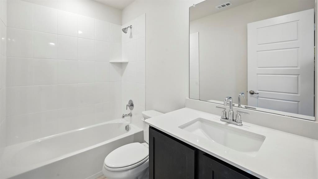 412 Carthage Street Caddo Mills, TX 75135 - Photo 27 of 32 Bathroom featuring a white bathtub with subway tile surround, a built-in shower shelf, a dark wood-finish vanity with an integrated sink, and a large wall-mounted mirror