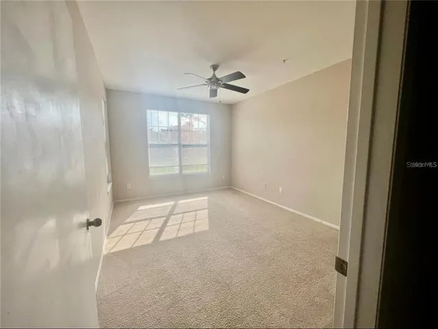 an empty room with chandelier fan and windows