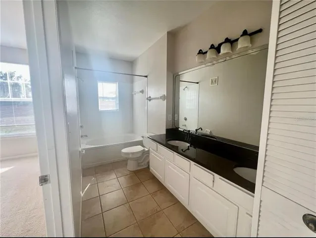 a spacious bathroom with a granite countertop sink a toilet a mirror and shower