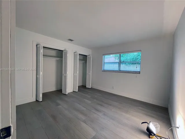 an empty room with wooden floor closet and windows