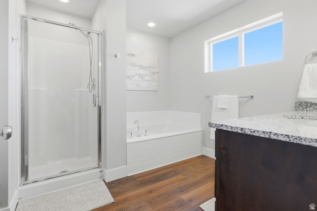 28 East Ginger Gold Road Santaquin, UT 84655 - Photo 33 of 36 Glass-enclosed shower, built-in soaking tub, wood-finish flooring, dark wood-finish vanity, and speckled countertop
