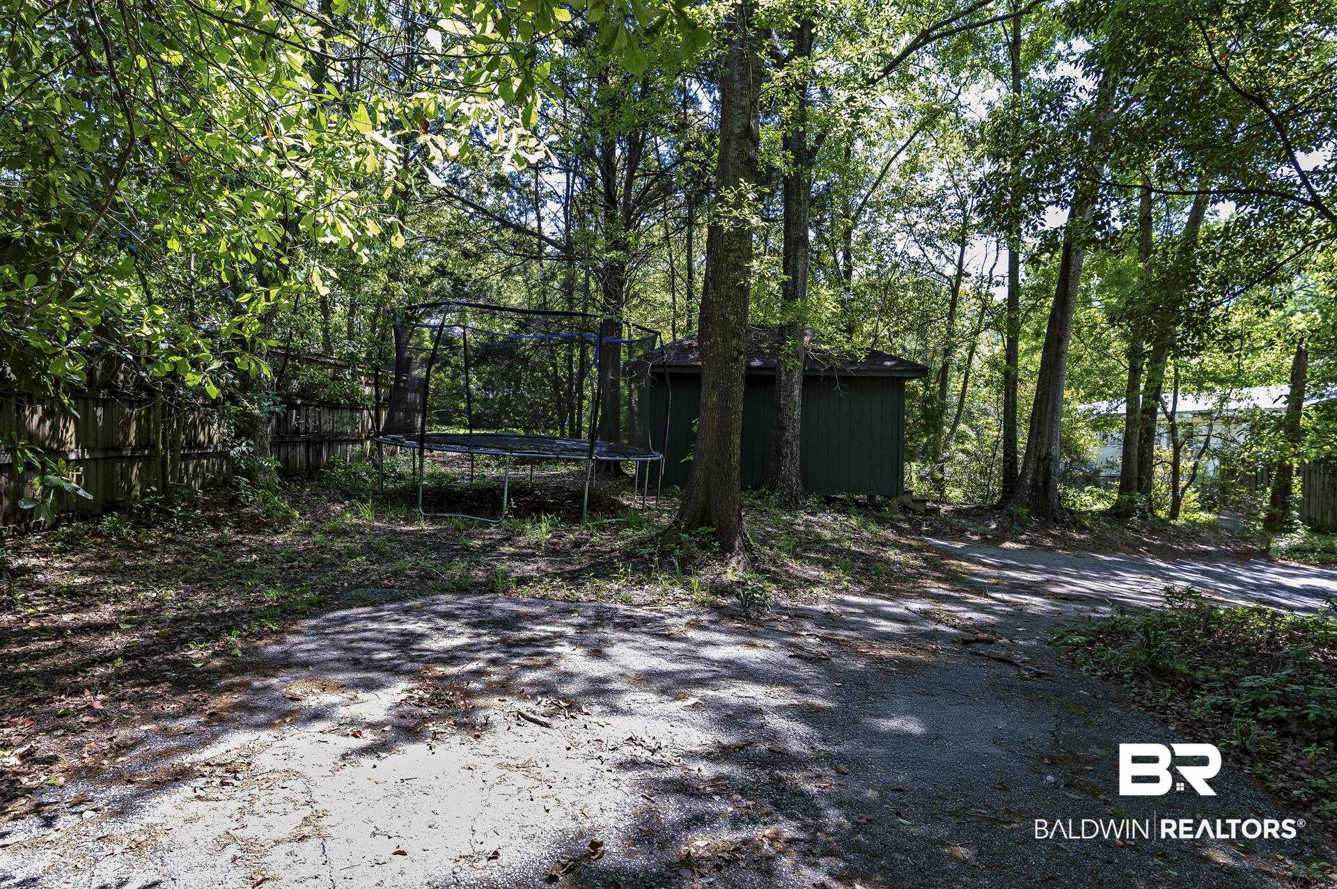 707 Johnson Avenue Fairhope, AL 36532 - Photo 11 of 38 Exterior space featuring a trampoline, a shed, fence, and an outbuilding