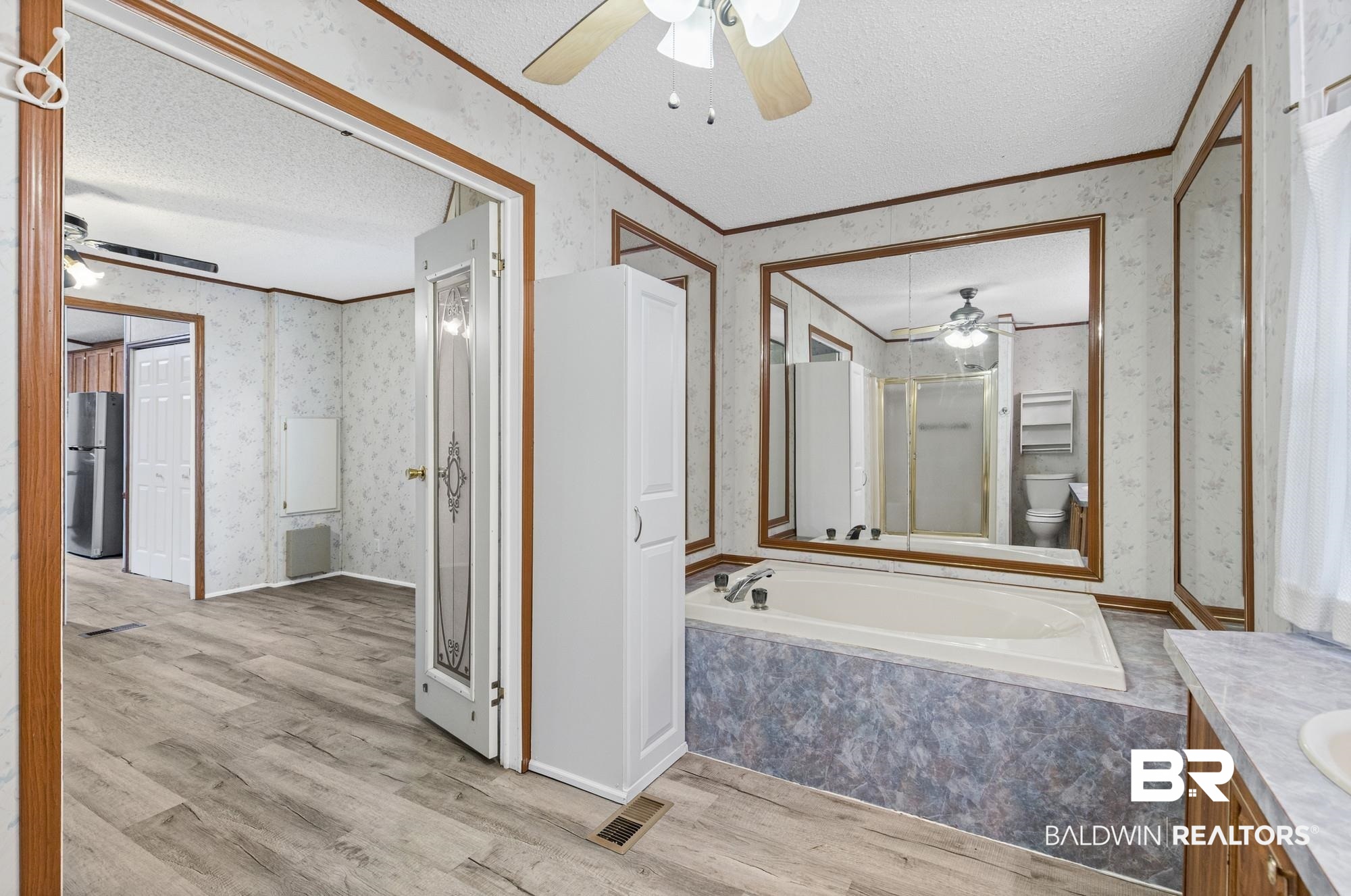 8675 Hunters Pointe Drive North Theodore, AL 36582 - Photo 13 of 20 Spacious bathroom featuring a built-in tub, extensive mirrored walls, wood-finish flooring, a ceiling fan, and built-in cabinetry