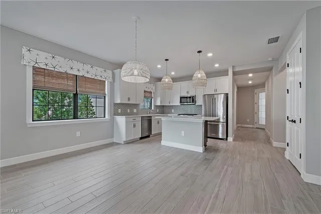 a large kitchen with kitchen island a large window a sink stainless steel appliances and cabinets