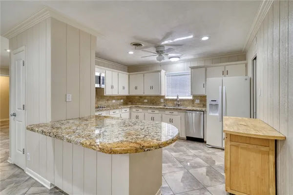 a kitchen with kitchen island granite countertop a stove a sink a refrigerator and white cabinets with wooden floor