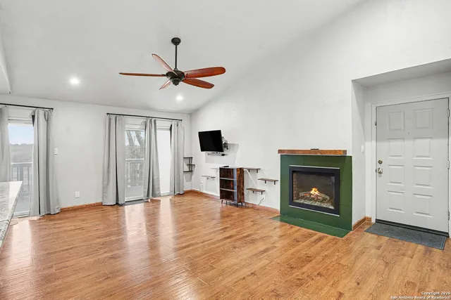 a view of a livingroom with a fireplace a ceiling fan and a kitchen view