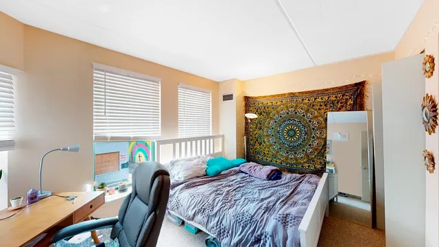 a bed sitting in a bedroom next to a window with computer on a desk