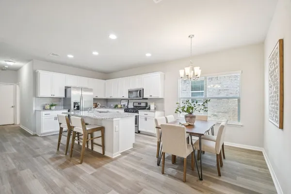 a kitchen with a dining table chairs wooden floor cabinets and appliances