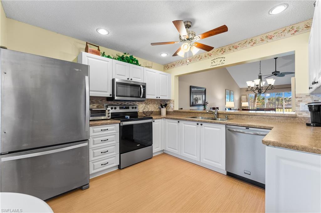 5928 Cranbrook Way, Unit D202 Naples, FL 34112 - Photo 4 of 23 Kitchen with a sink, ceiling fan with notable chandelier, light wood-style floors, backsplash, and appliances with stainless steel finishes