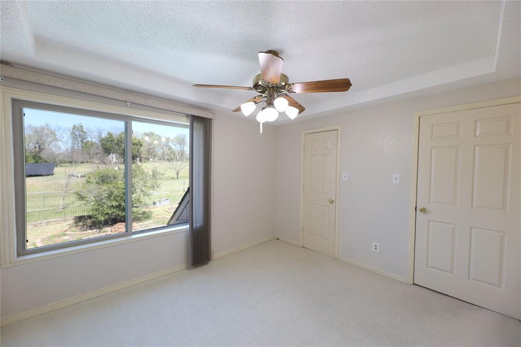 907 Red Oak Creek Road Ovilla, TX 75154 - Photo 16 of 20 Spacious room featuring a tray ceiling, ceiling fan with light fixture, light-colored carpeting, multiple paneled doors, and a large window overlooking green spaces