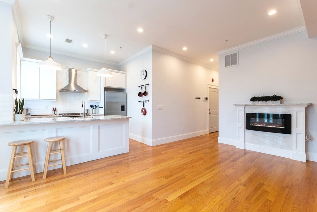a large kitchen with granite countertop a stove a sink a refrigerator and white cabinets with wooden floor